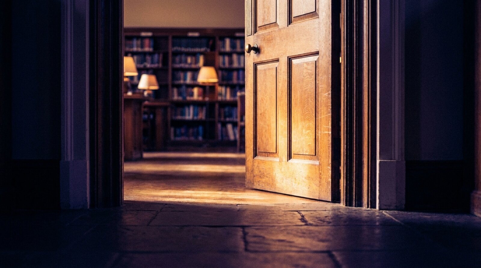A heavy library reading-room door standing open, warm light spilling through onto a dark stone floor