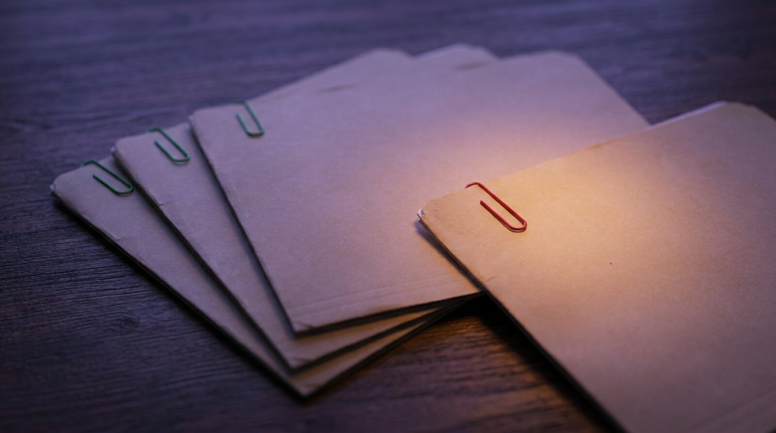 Five folders fanned on a table, four clipped in green and one in red